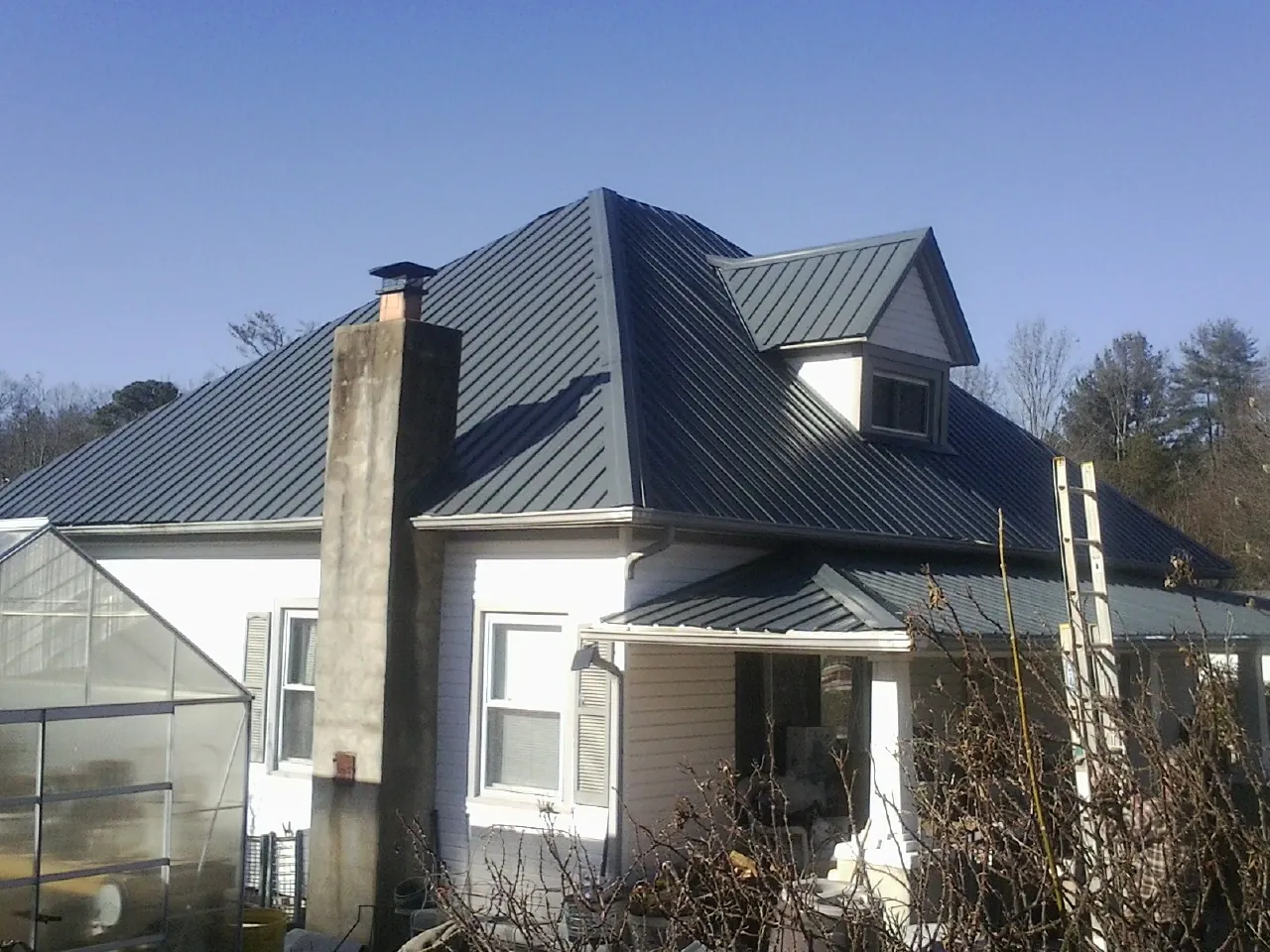 Dark blue standing seam metal roof on a white farmhouse with dormer — Slate & Tile Roof Repair by Roofing Brothers in Moorhead