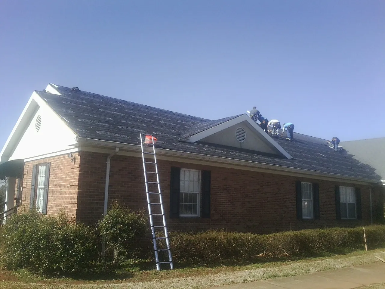 Crew tearing shingles off a brick ranch roof with a ladder set — Emergency Roof Repair work by our crew in Moorhead