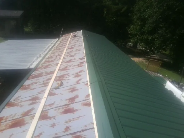 Old rusted panels beside newly installed green metal roofing — Wind Damage Roof Repair by Roofing Brothers in Moorhead