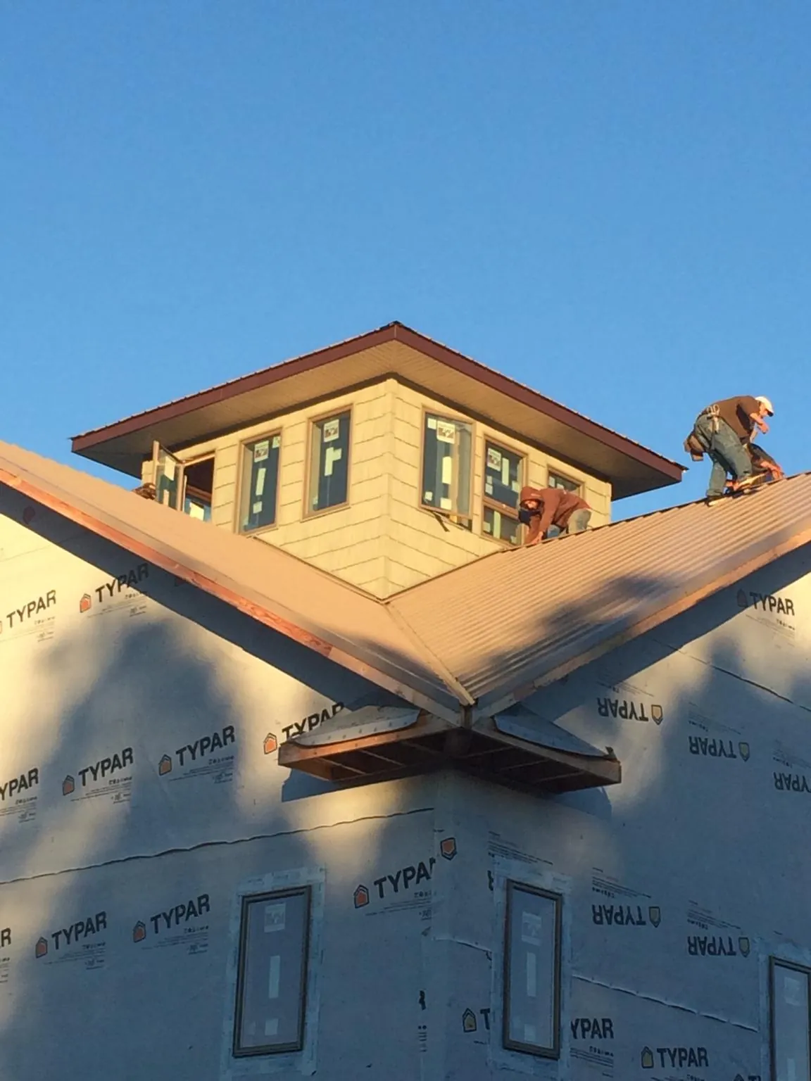 Roofers working around a rooftop cupola on a new metal roof at sunset — Roof Waterproofing in Moorhead by Roofing Brothers